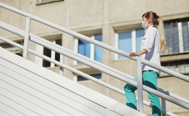 Female doctor or nurse in a protective face mask walking up the stairs