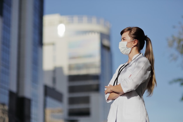 Female doctor, nurse wearing a protective face mask in the city. Skyscraper, sky