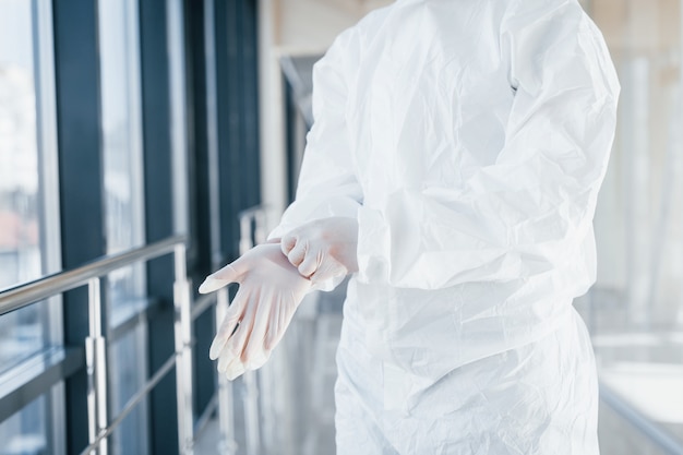 Female doctor scientist in lab coat, defensive eyewear and mask standing indoors and wearing gloves