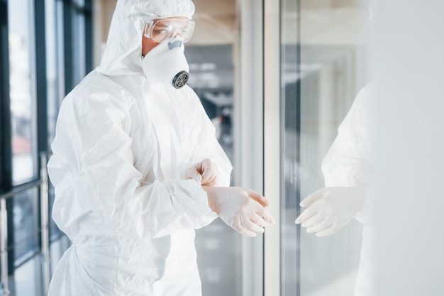 Female doctor scientist in lab coat, defensive eyewear and mask standing indoors and wearing gloves