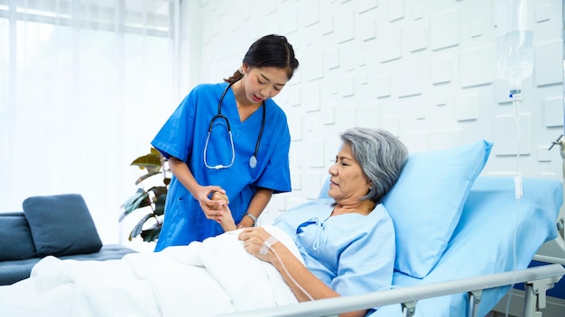 Female doctor specializing in physical therapy came to check the body of an elderly female patient lying on the bed receiving saline in the patient room