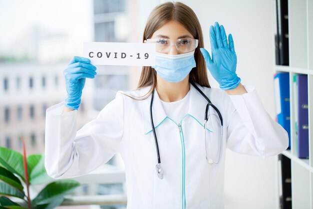 Female doctor in uniform holding a paper signboard lettering covid