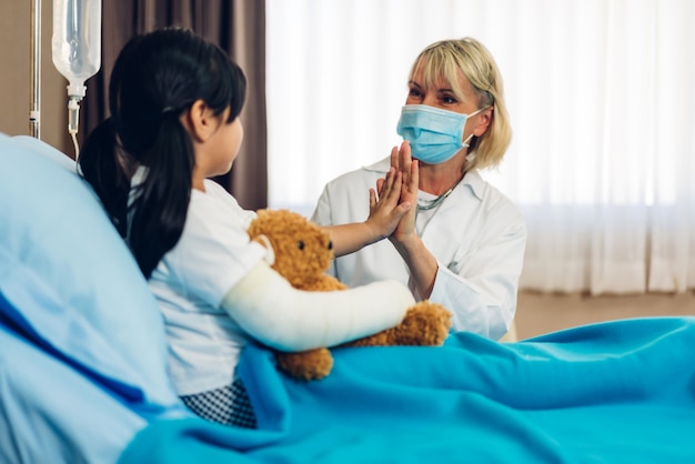 Female doctor wearing mask talking with little patient