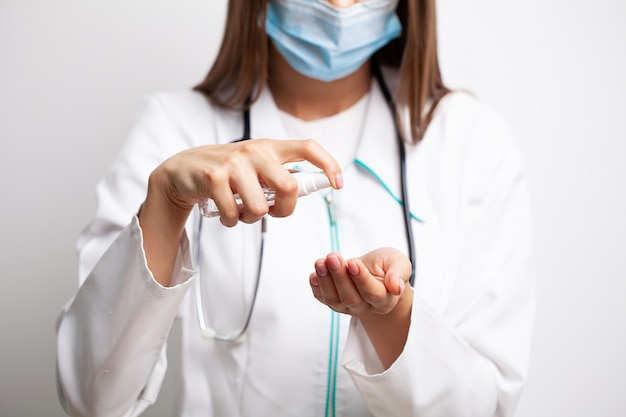 Female doctor in a white coat disinfects her hands with antiseptic