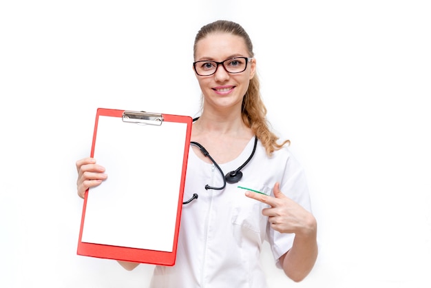 Female doctor in white coat holds a clipboard and points at it isolated on white background