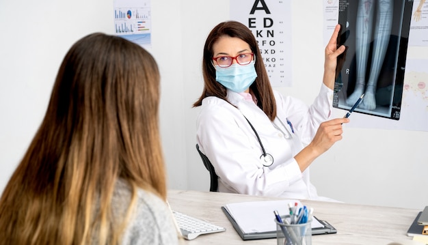 Female doctor with mask attending to a patient in her consultation showing x-ray