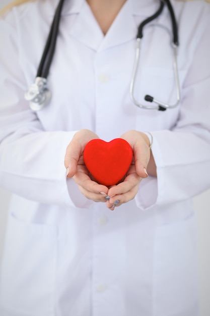 Female doctor with stethoscope holding heart.  Patients couple sitting in the background