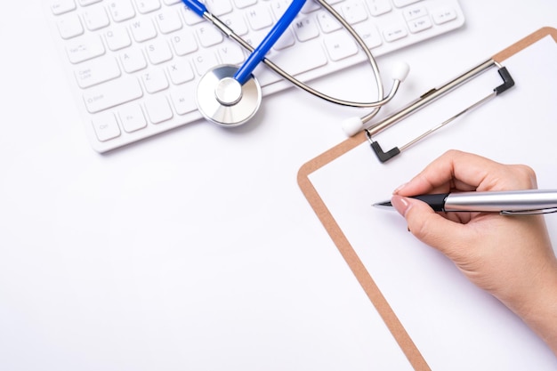 Photo female doctor writing a medical record case over clipboard on white working table with stethoscope computer keyboard top view flat lay copy space