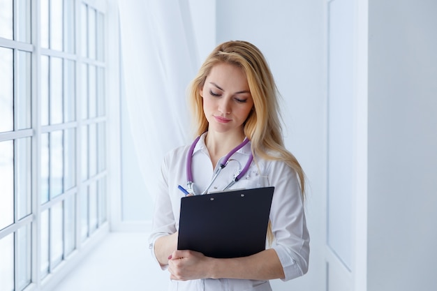 Female doctor writing a prescription. Cute nurse girl hold in hand pen with a stethoscope around his neck.