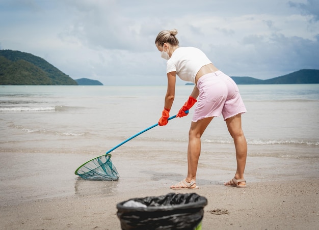 A female ecologist volunteer cleans the beach on the seashore from plastic and other waste