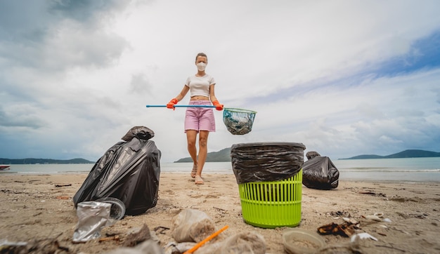 A female ecologist volunteer cleans the beach on the seashore from plastic and other waste