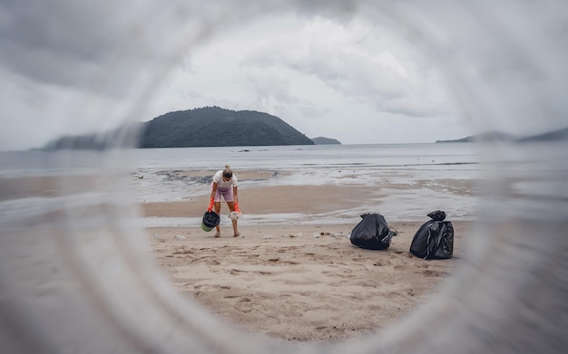 A female ecologist volunteer cleans the beach on the seashore from plastic and other waste