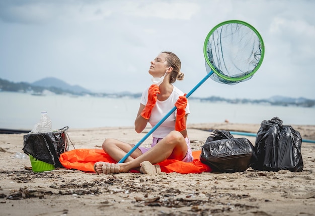 A female ecologist volunteer is resting after cleaning the beach on the seashore from plastic and other waste