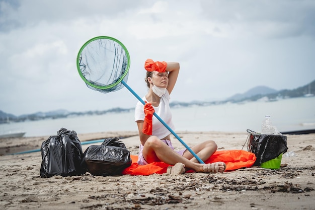 A female ecologist volunteer is resting after cleaning the beach on the seashore from plastic and other waste