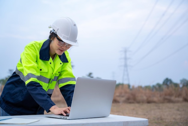 A female electrical engineers using a notebook computer standing at power station to view the planning work by producing electrical energy at high voltage electrodes