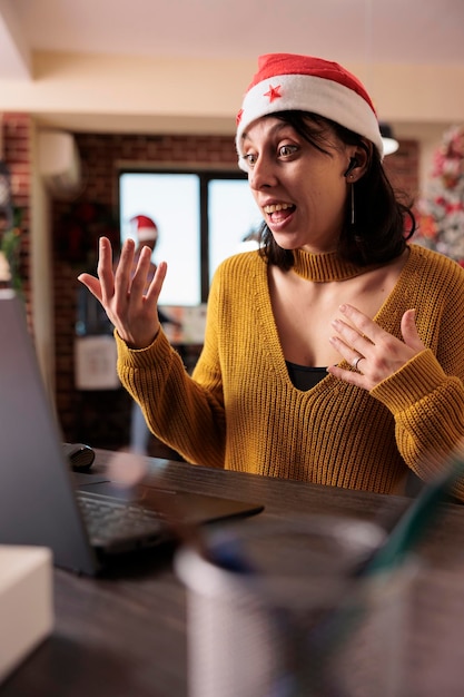 Female employee chatting on videocall meeting at job, talking on remote videoconference call in office with christmas tree. Woman using teleconference chat in festive workplace.