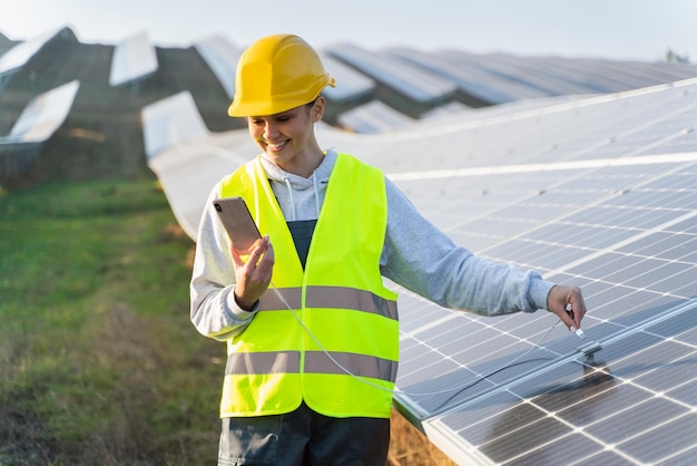 Female engineer feeling happy while charging mobile phone from solar panels She working on maintenance of contemporary photovoltaic panels on solar power station