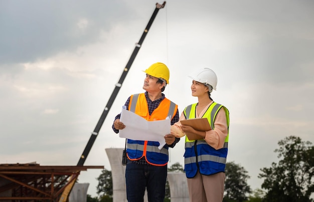 Female engineer and foreman worker checking project at building site Engineer and builders in hardhats discussing on construction site Teamwork concepts