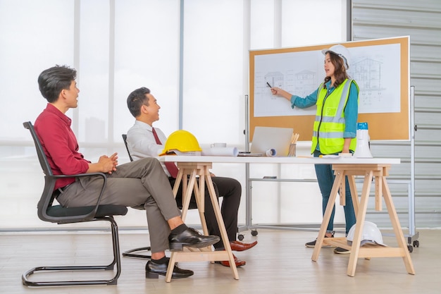 Female engineer is presenting building plan drawing to her contractor team and client