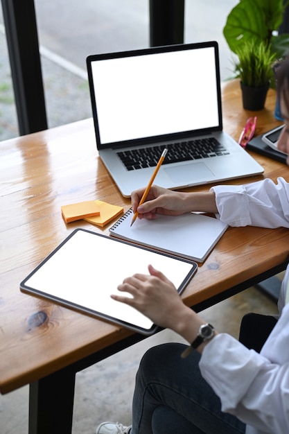 Female entrepreneur working with digital tablet and making note on notebook.