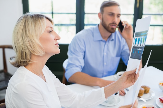 Female executive looking at document while colleague talking on mobile phone