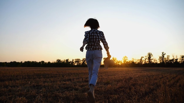 Female farmer running through the barley plantation at sunset Agronomist jogging among wheat meadow at dusk Beautiful scenic landscape Concept of agricultural business Close up Slow motion