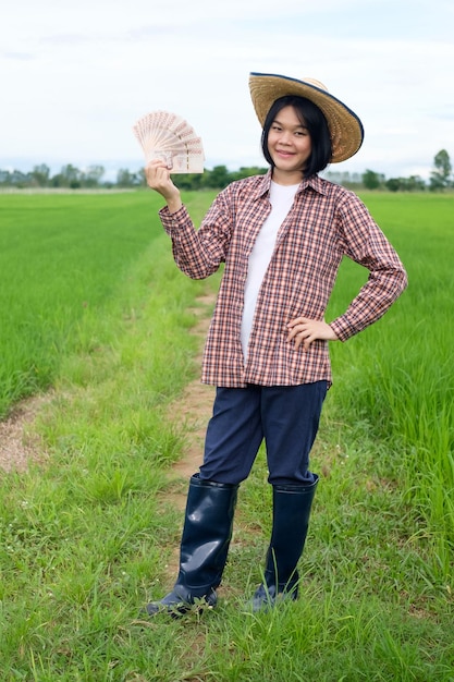 Female farmer wear hat posing with banknotes smiling in a rice field