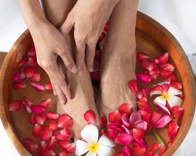 Female feet and hands  in  wooden bowl with flowers at spa salon.