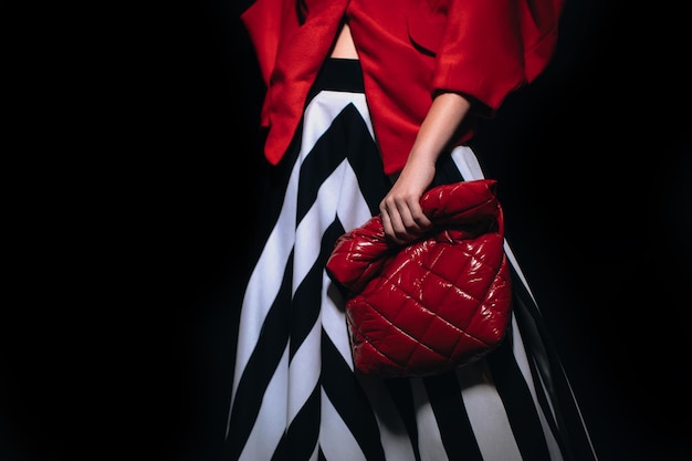 Female figure dressed in a stylish striped black white skirt and red jacket holding leather  handbag