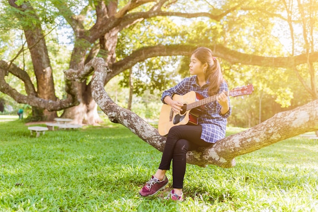 Female fingers playing guitar outdoor in summer park.