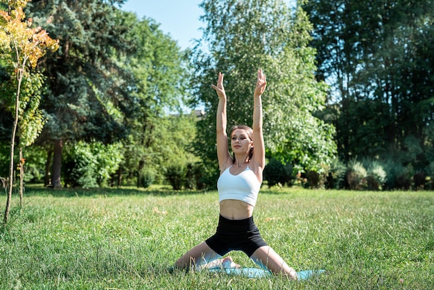 Female fitness trainer doing morning yoga exercises in green grass at park Summer time for sport