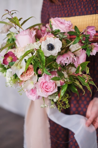 female florist holding a freshly made blooming floral bouquet of pastel against a gray wall.