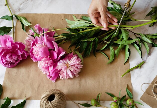 A female florist makes a bouquet of peony flowers wrapped in kraft paper on her desktop View from above High quality photos