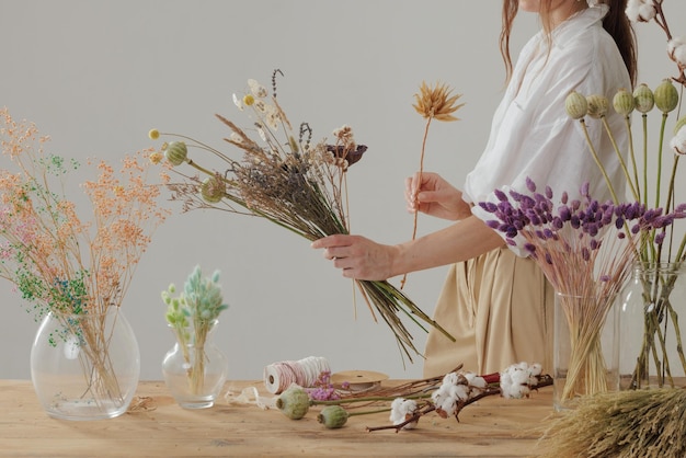 A female florist makes an everlasting bouquet of dry flowers at a wooden table in her workshop