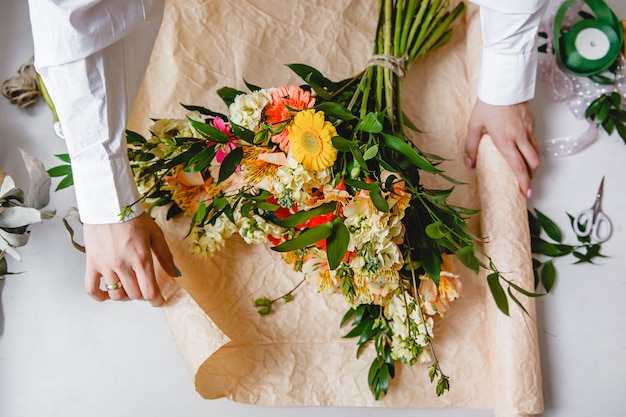 A female florist in a white shirt wraps a bouquet of fresh flowers in paper