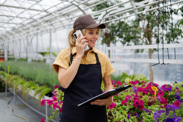 Female flower greenhouse worker with clipboard talking on the phone