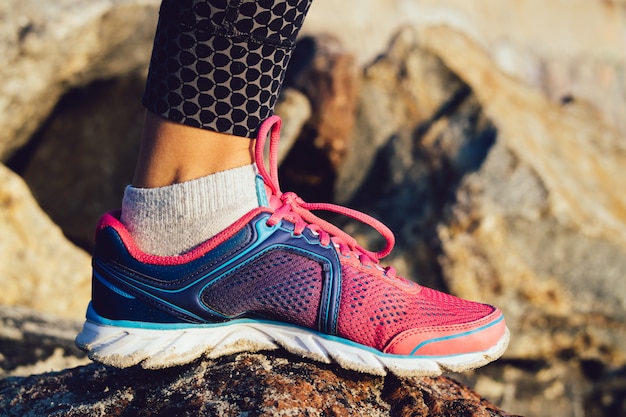 Female foot in pink and blue sneaker standing on rocky stones sunny morning