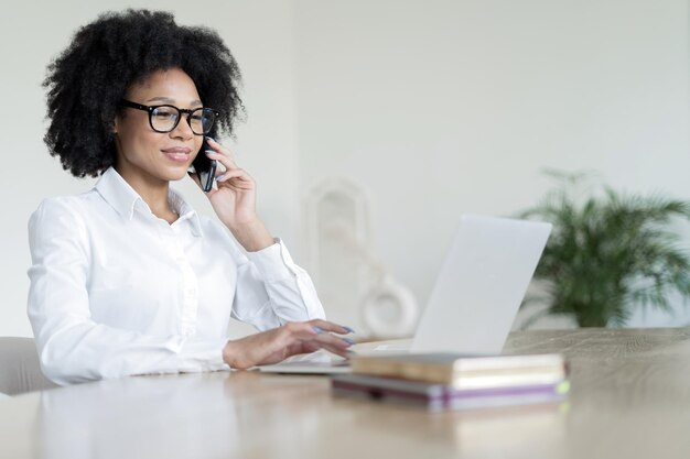 A female freelancer talks on the phone works online in the office uses a laptop