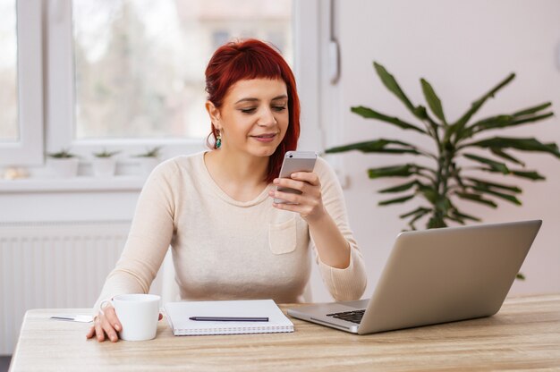  female freelancer working from home, young hipster girl using modern smartphone device while sitting at home and communicate with friends, lifestyle concept