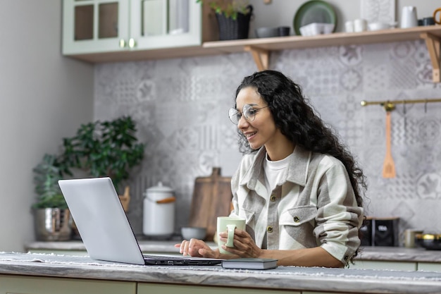 Female freelancer working remotely from home hispanic woman in glasses and curly hair using laptop