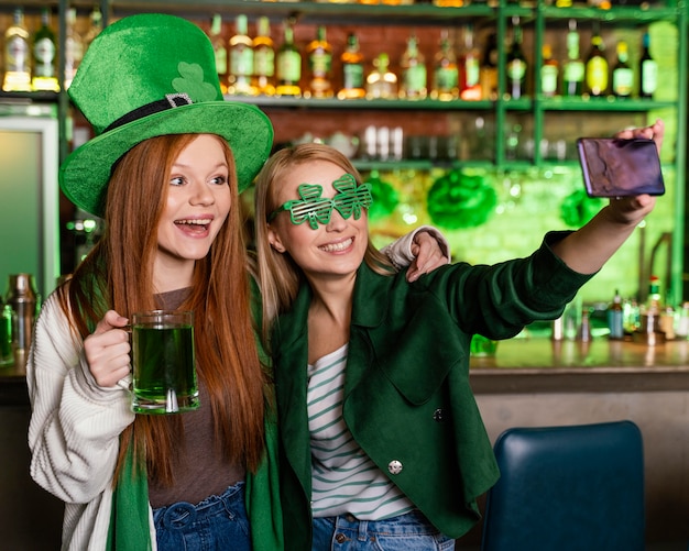 Female friends celebrating st. patrick's day at the bar and taking selfie together