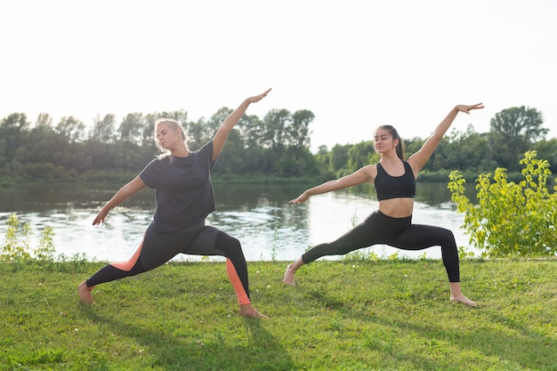 Female friends enjoying relaxing yoga outdoors in the park.