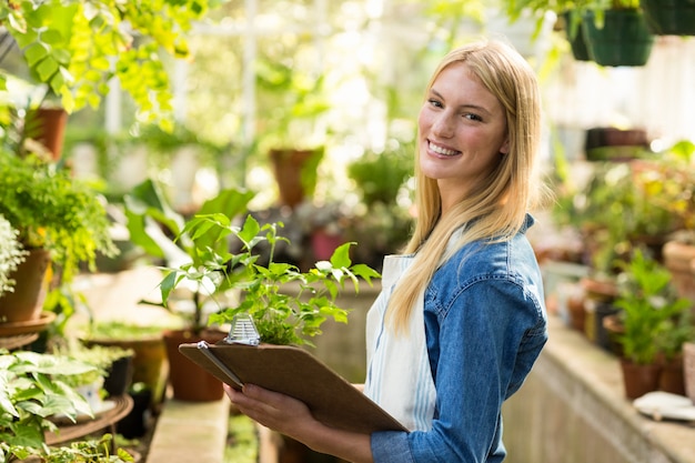 Female gardener holding clipboard while examining plants