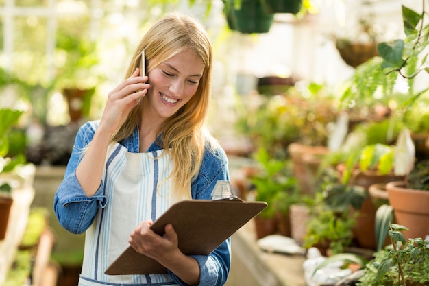 Female gardener talking on cellphone while looking at clipboard