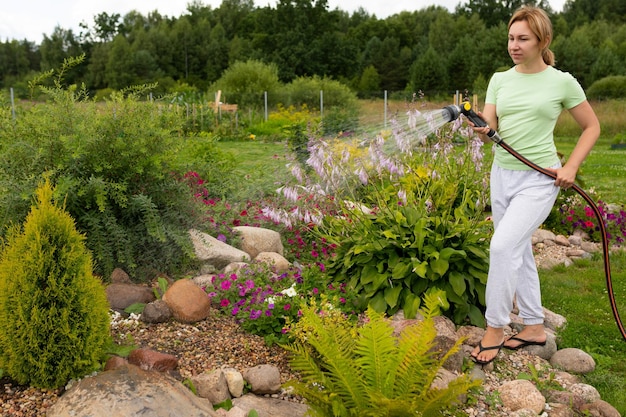 Female gardener watering flowers in a flower bed with a garden hose