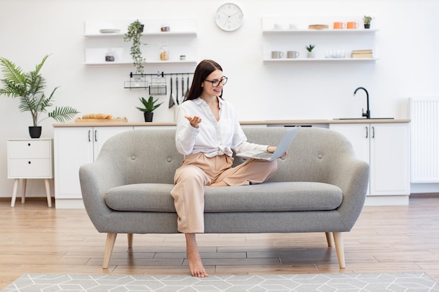 Female gesturing with hands while sitting on couch with modern laptop