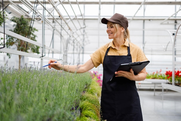 Female greenhouse worker with clipboard inspects flowers