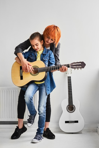 Female guitarist teaching kid during lesson in light studio