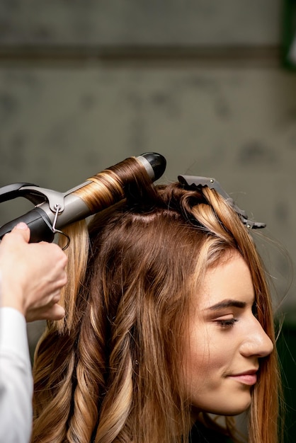 The female hairdresser is curling hair for a brownhaired young caucasian woman in a beauty salon