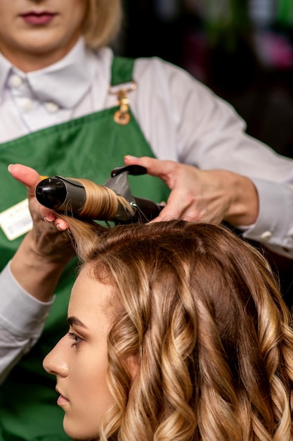 The female hairdresser is curling hair for a brownhaired young caucasian woman in a beauty salon